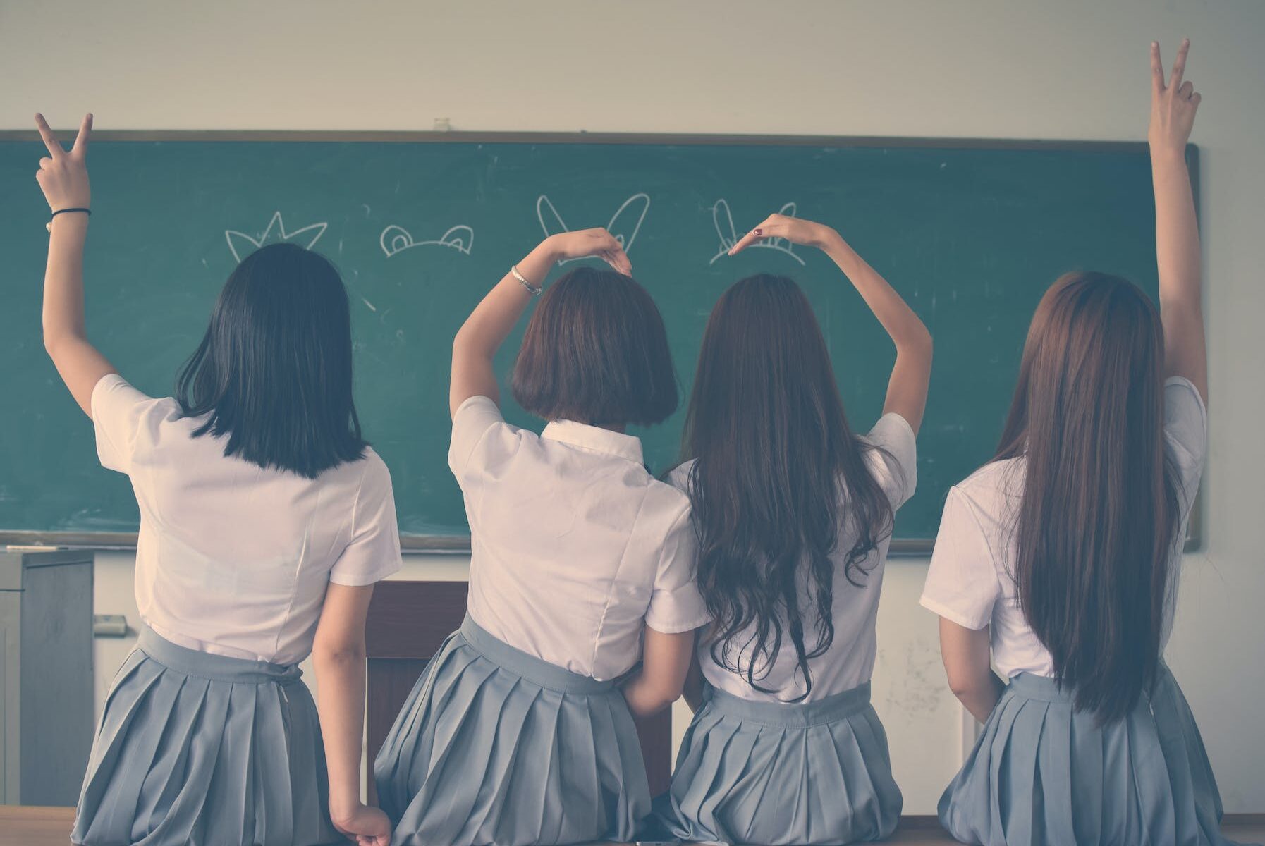 photo of four girls wearing school uniform doing hand signs